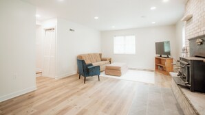 Ein geräumiges Wohnzimmer mit einem beigefarbenen Sofa, einem blauen Sessel, einem Holztisch und einem Kamin.