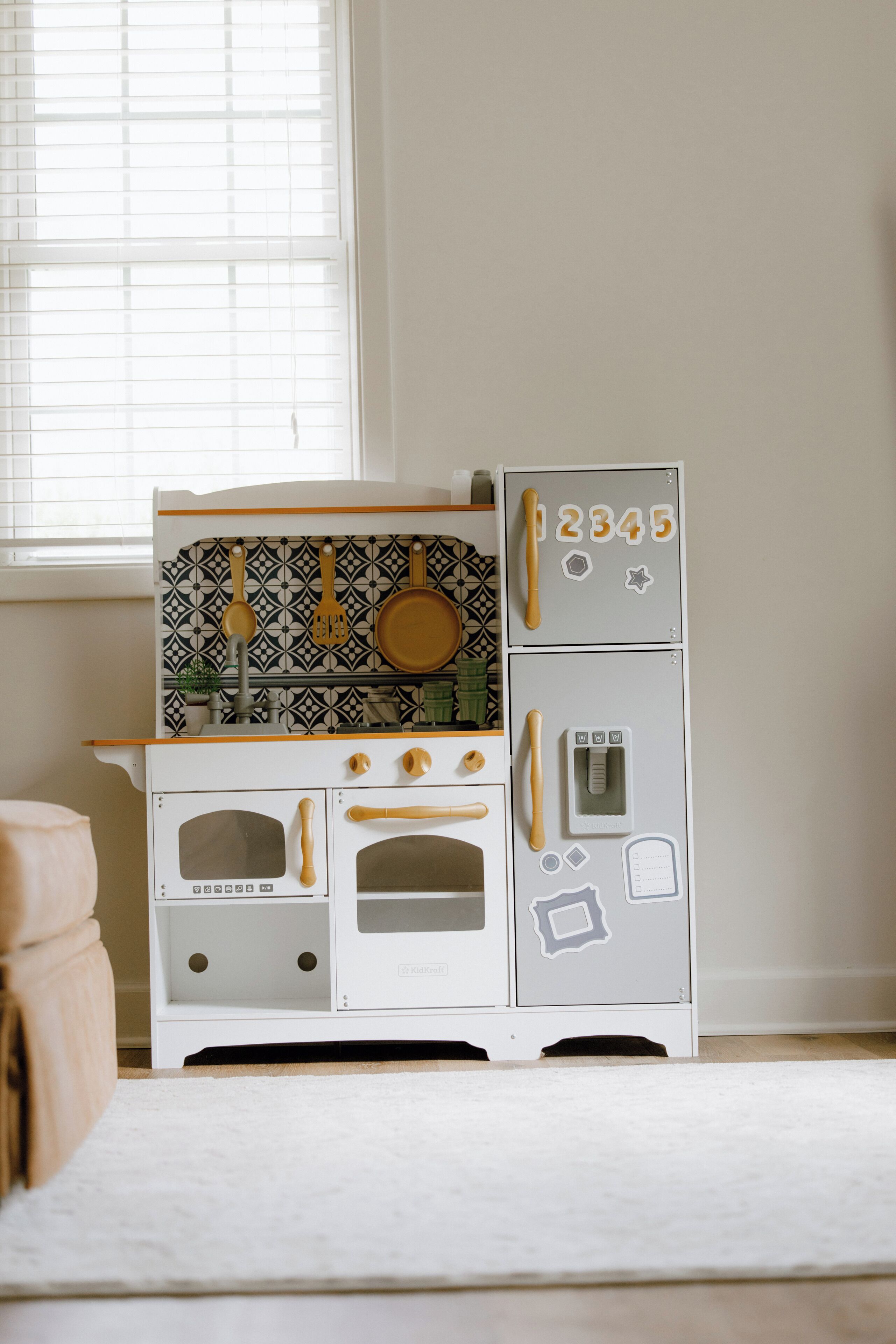 Uma cozinha de brincadeira infantil com painel de fundo estampado, fogão, forno e geladeira.