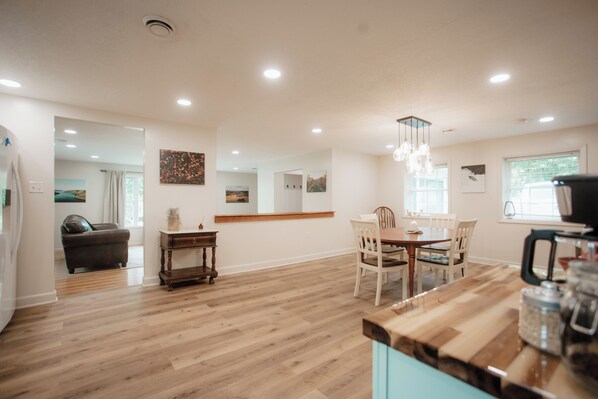 Une cuisine spacieuse avec un plancher en bois, un coin repas avec des chaises blanches et un lustre moderne.