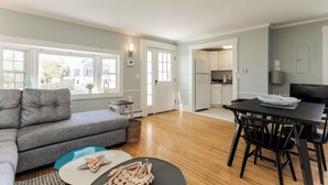 Un salon moderne avec un canapé gris, une table à manger avec des chaises, et un coin cuisine à l’arrière-plan.