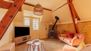 Een loft-achtige kamer met zichtbare houten balken, een flatscreen televisie, een roze bank, een open haard en een groot raam.