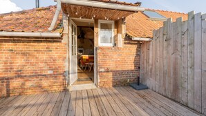 Een gebouw van baksteen met een houten terras, een houten hek en een pannendak.