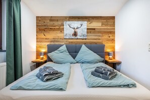 A double bed with two pillows, a wooden headboard, a framed deer picture, bedside lamps, and folded towels.