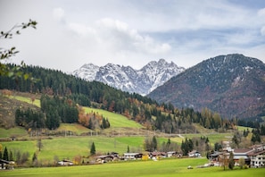 Un paysage rural avec une chaîne de montagnes, des maisons et un champ verdoyant.