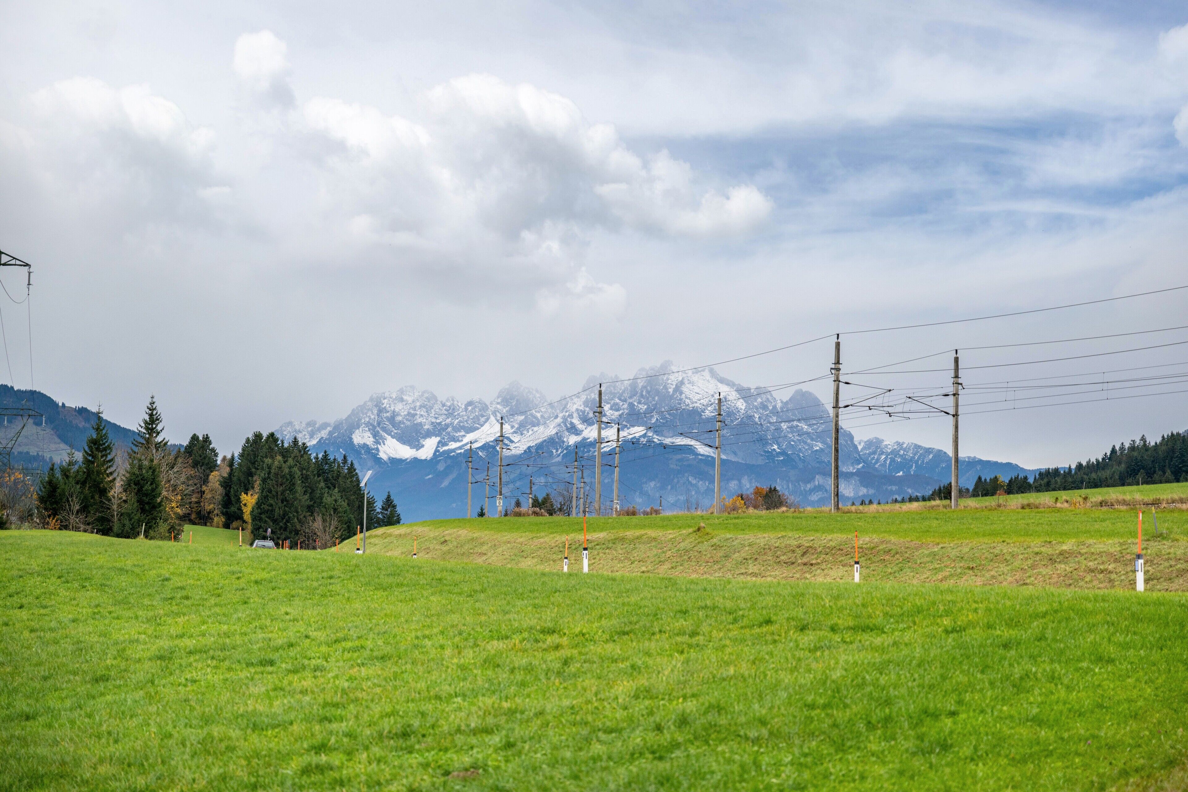 Un champ verdoyant, avec une chaîne de montagnes en arrière-plan, des poteaux électriques et un ciel dégagé.