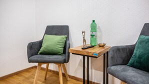 Two grey armchairs with green cushions, a wooden side table with a remote control, a bottle, and a small bowl.