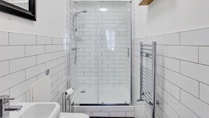 Un bagno moderno con pareti piastrellate di bianco, cabina doccia in vetro, lavabo bianco e porta asciugamani.