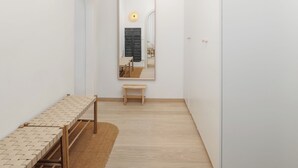 Una stanza dal design minimalista con una lunga panca intrecciata, uno sgabello di legno e uno specchio, con un punto luce a parete.