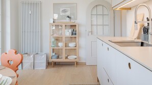 Una cucina moderna con mobili bianchi, un armadio in legno pieno di stoviglie, un termosifone e una finestra ad arco.