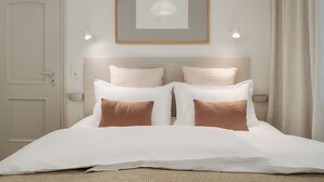 Un letto rifatto con cura, coperto da biancheria bianca e marrone, con un quadro incorniciato sopra e una porta sul lato sinistro.
