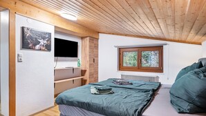 Un dormitorio con cama, televisor, ventana y techo de madera.