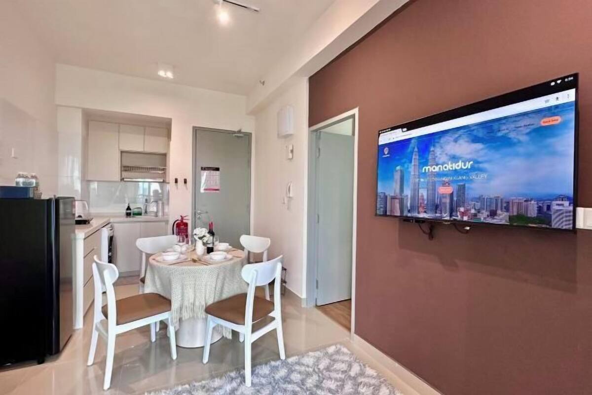 A modern kitchen with white cabinets, a dining area with a round table and chairs, and a TV mounted on the wall displaying a cityscape.