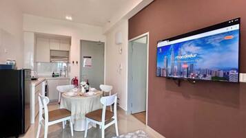 A modern kitchen with white cabinets, a dining area with a round table and chairs, and a TV mounted on the wall displaying a cityscape.