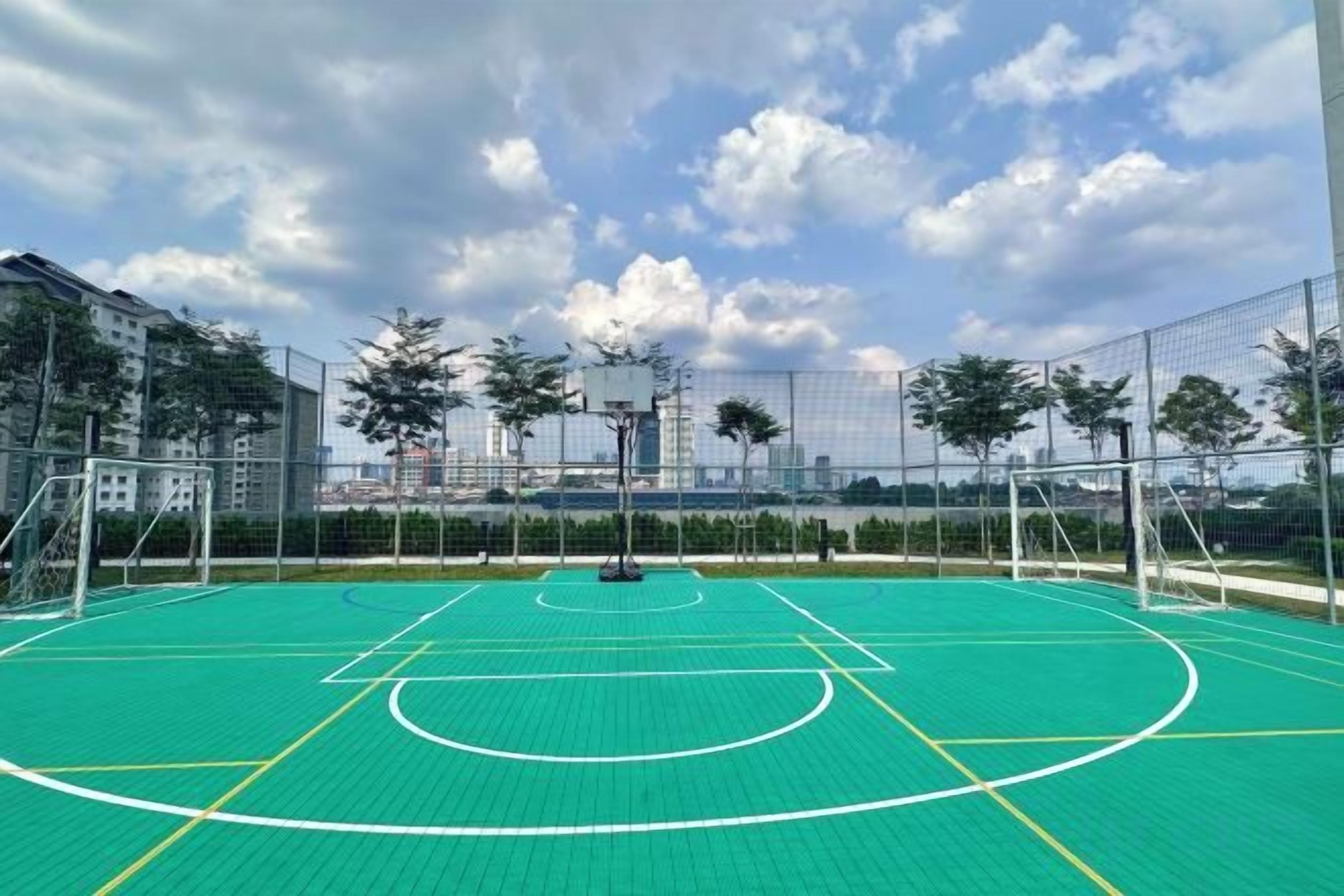 Una cancha de baloncesto al aire libre con aro, rodeada por una cerca y árboles al fondo.