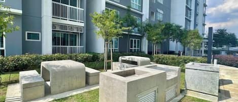 A courtyard with concrete seating, a small tree, and a building with multiple windows and balconies in the background.