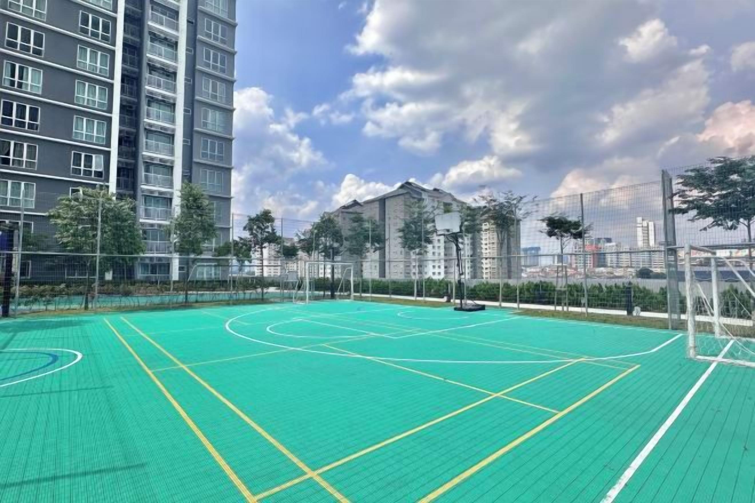 An outdoor basketball court surrounded by a fence, with residential buildings in the background.