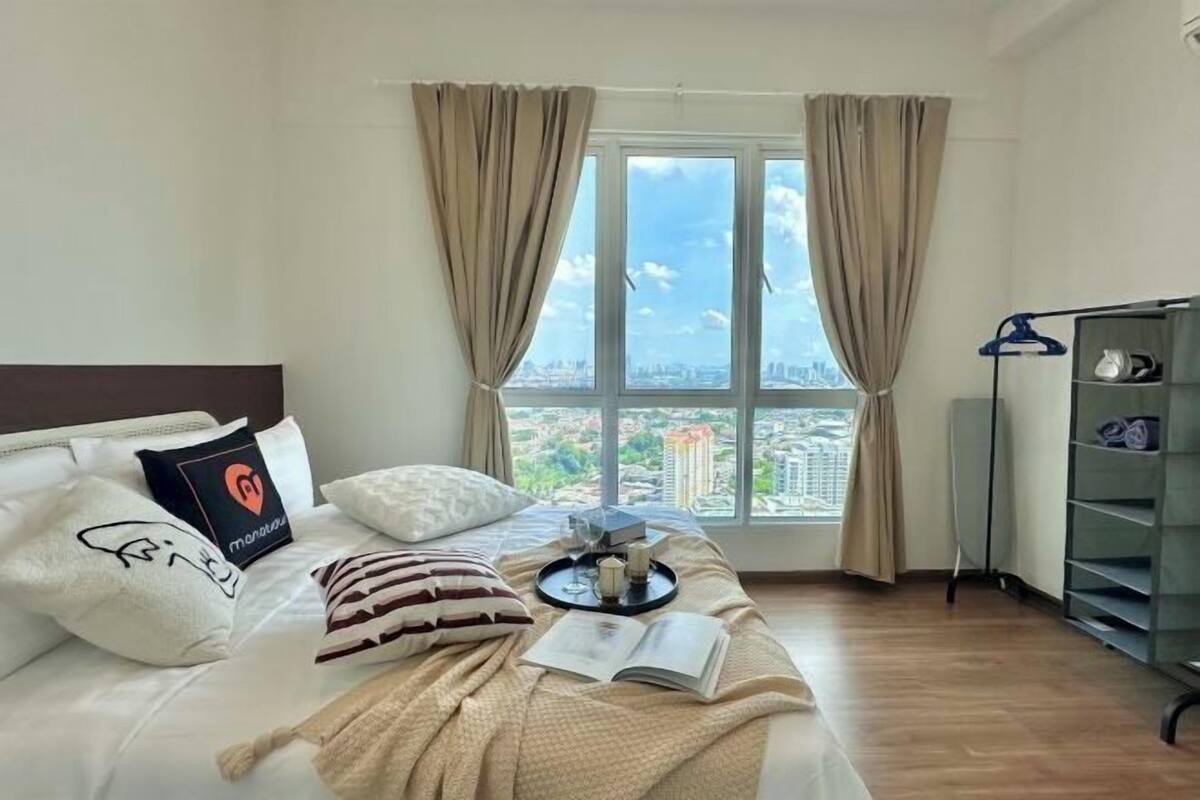 Habitación de hotel con cama, ventana con cortinas, bandeja con objetos y vista a un paisaje urbano.