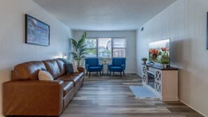 A modern living room with a brown leather sofa, two blue armchairs, a small table, and a TV on a wooden cabinet.