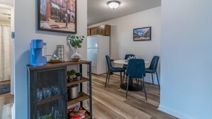 A modern kitchen with a refrigerator, coffee machine, and dining area with chairs and a table.