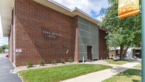 A brick building with "Park Manor Arts" signage, a clear sidewalk, and a tree.