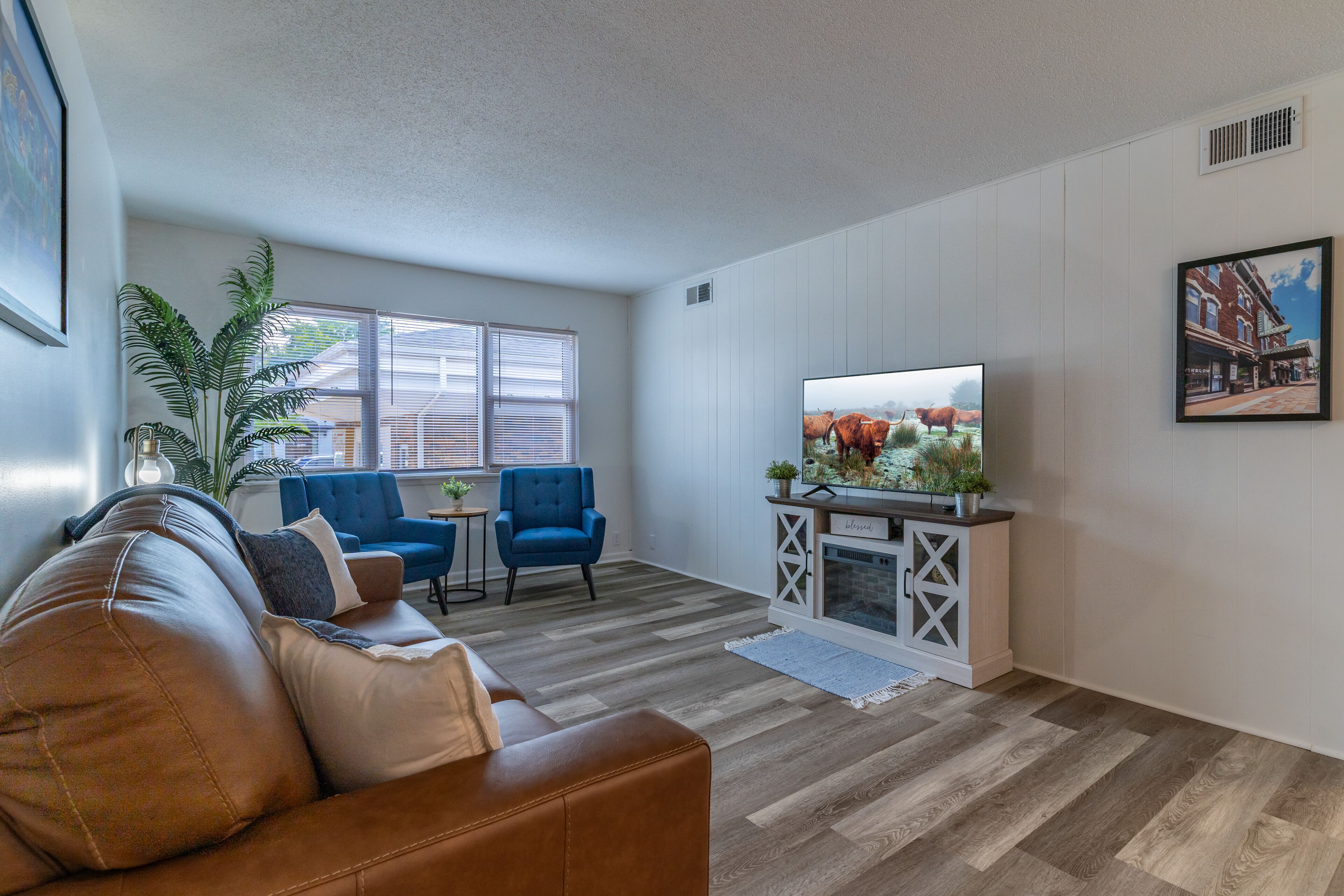 A living room with a brown leather couch, blue chairs, a TV, a fireplace, and a large window.