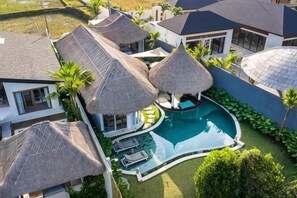 Ein Resort mit mehreren Gebäuden, einem Swimmingpool und strohgedeckten Strukturen.