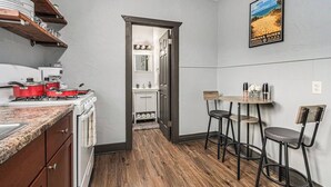 A kitchen with a stove, pots, and a coffee machine. There is a small dining area with a table and chairs. A poster of a beach is on the wall. - Luxe Michigan City Getaway-Private-Unit A (Michigan City)