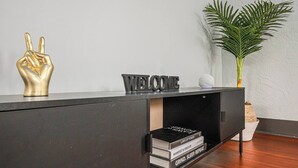 A modern black console table with a 'WELCOME' sign, a decorative gold hand sculpture, and a potted plant. - Luxe Michigan City Getaway-Private-Unit A (Michigan City)
