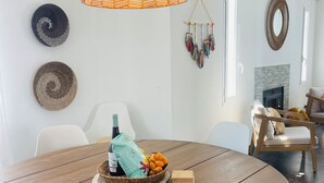 A dining area with a round wooden table, white chairs, a woven pendant light, and decorative wall art. - Casa Bonic: Villa with Sunset - seaview and pool (Sant Josep de sa Talaia)