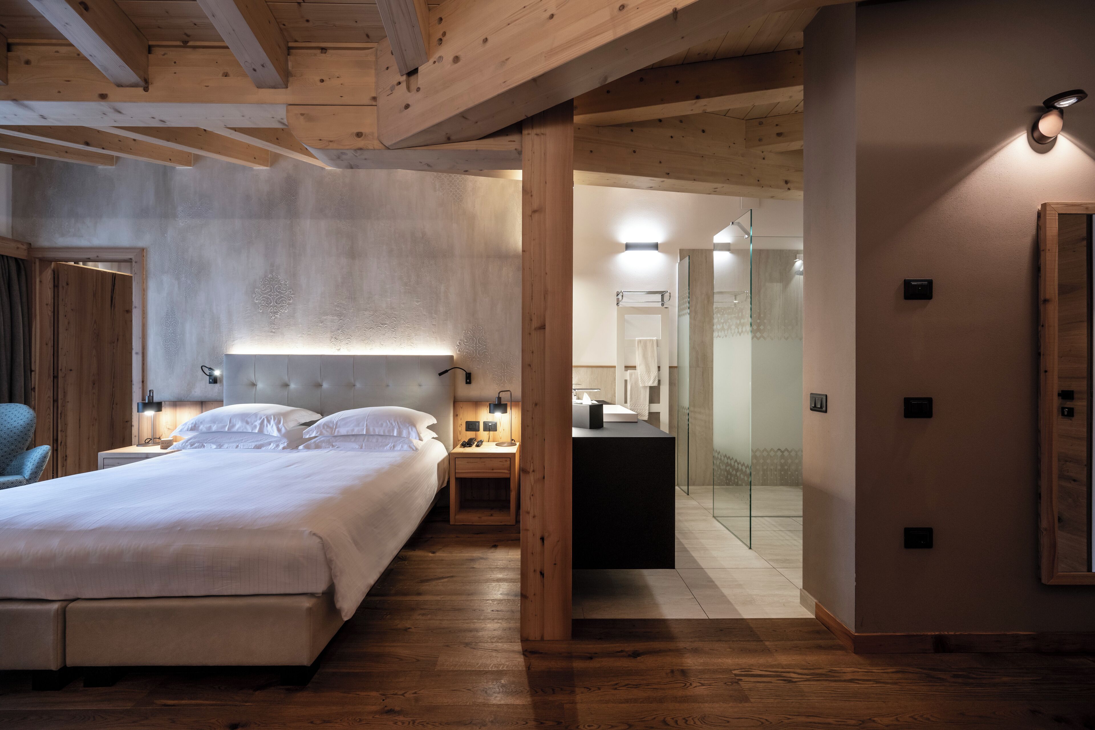 A hotel room with a bed, bedside tables, a mirror, and a wooden ceiling.