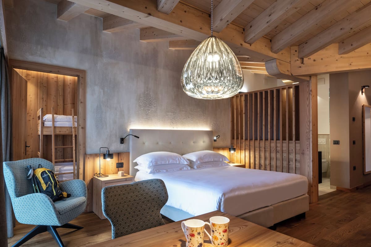 Ein modernes Schlafzimmer mit einem großen Bett, Holzbalkendecke, einer Hängeleuchte und einem Nachttisch mit Lampe.