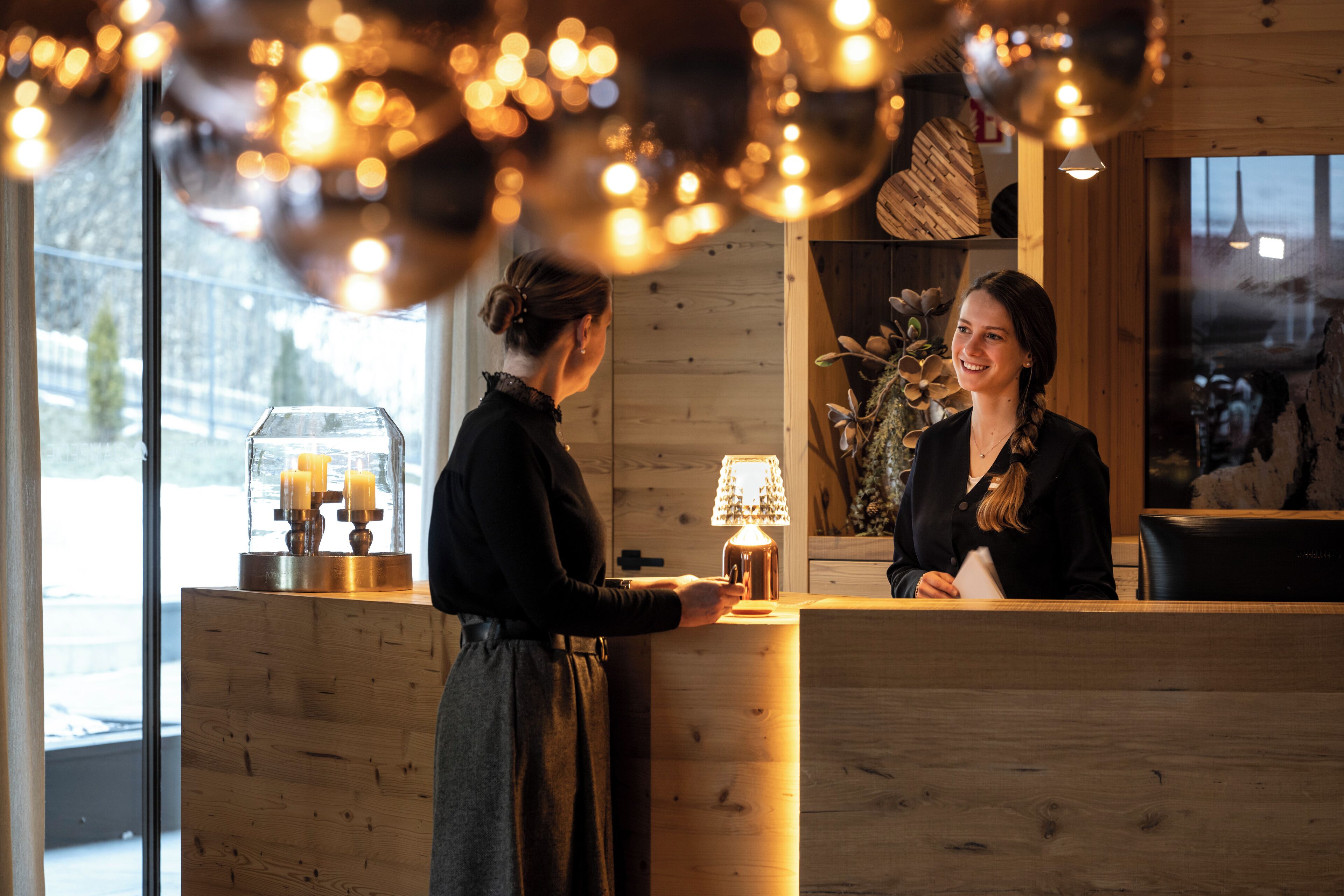 A reception desk with a wooden finish, a glass display case with candles, and a warm light fixture above.