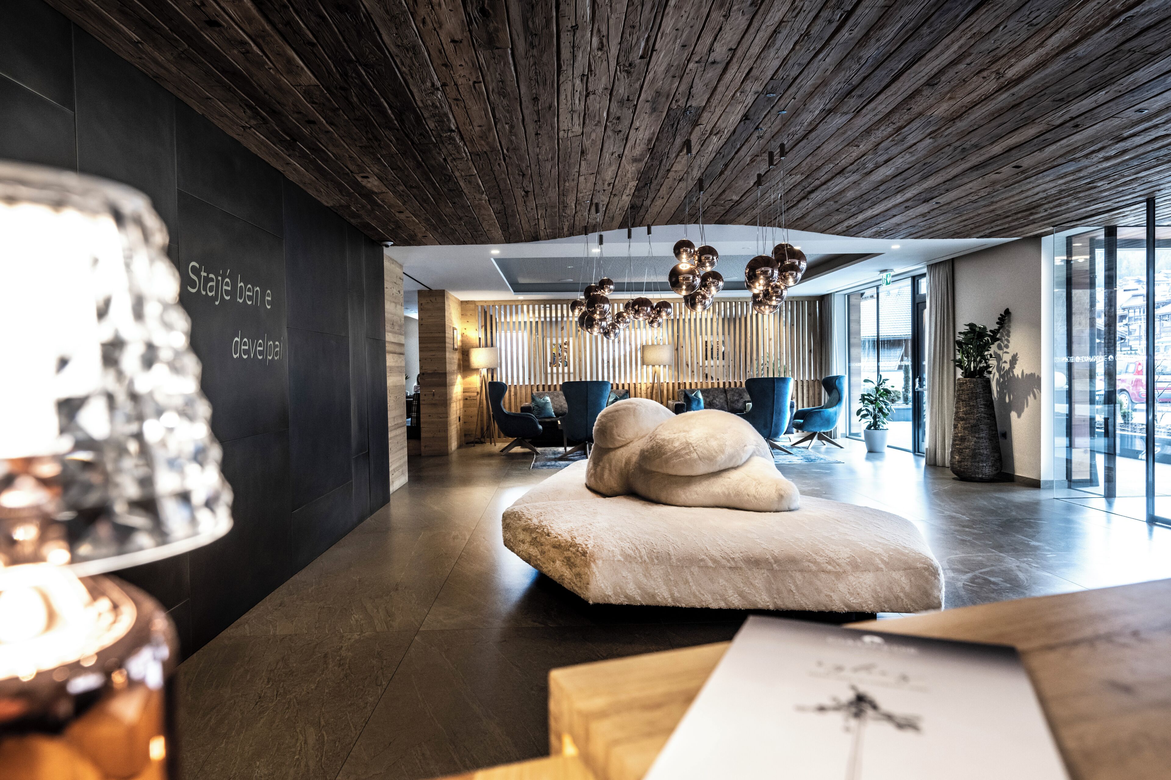 A modern interior with a wooden ceiling, a seating area with a white pouf, and a large window providing a view.