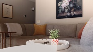 A living room with a sofa, a coffee table with a remote control, a potted plant, and a painting on the wall. - Quiet Escape- Family Getaway by Trails and Shopping (Tucson)