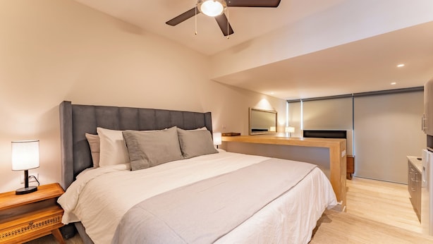 Ein modernes Schlafzimmer mit einem großen Bett, einem Deckenventilator, einem Nachttisch mit Lampe und einem eingebauten Schreibtisch mit Spiegel.