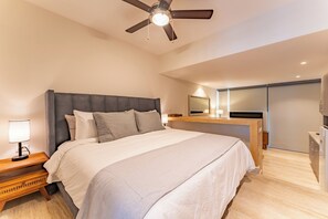 Ein modernes Schlafzimmer mit einem großen Bett, einem Deckenventilator, einem Nachttisch mit Lampe und einem eingebauten Schreibtisch mit Spiegel.