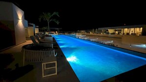 A nighttime swimming pool with blue lighting, lounge chairs, and a palm tree. - Ipana 1 Bedroom Full Equipped Oceanview Rooftop (Playa del Carmen)