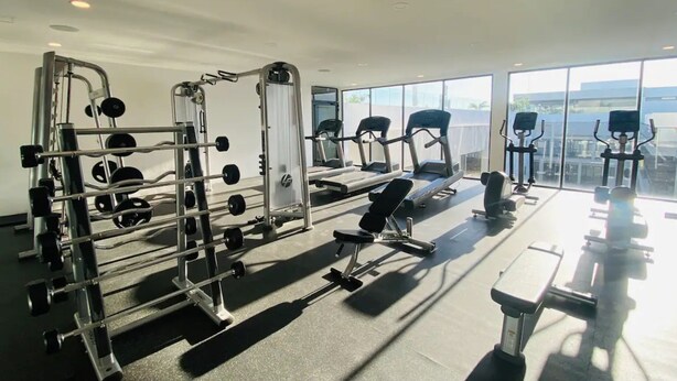A gym with various exercise equipment, large windows, and a view of the city. - Ipana 1 Bedroom Full Equipped Oceanview Rooftop (Playa del Carmen)