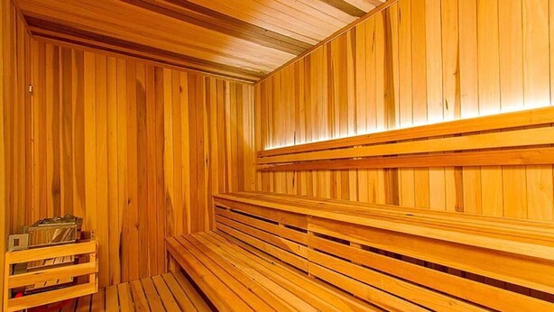 Una sauna con bancos y paredes de madera, un banco con un sujetabroche para toallas, y una pequeña mesa con objetos encima.