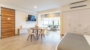 Una habitación de hotel moderna con comedor, sofá, televisor montado en la pared y armario.