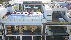 Un edificio moderno con piscina en la azotea, varios balcones y amplias ventanas.