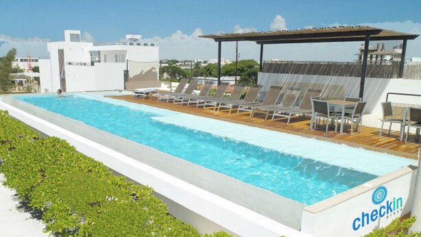 A swimming pool with lounge chairs and a covered area, surrounded by greenery and modern buildings. - Penthouse w Private Jacuzzi Steps to 5thav Beach (Playa del Carmen)