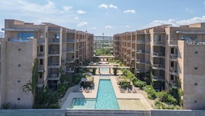 A modern hotel with a central pool, multiple balconies, and lush greenery.