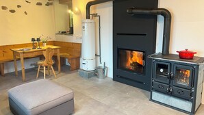 Um quarto aconchegante com um banco de madeira, uma mesa com luminárias, um aquecedor a gás e uma lareira a lenha.