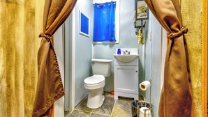 A bathroom with a toilet, sink, and blue shower curtain. - Squirrel Cabin at Panther Creek (Cherokee)