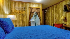A room with a large bed, a wooden wall, a window with curtains, a sink, and a television. - Squirrel Cabin at Panther Creek (Cherokee)