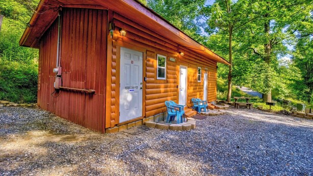 A wooden cabin with a gravel driveway, a door labeled "SECURITY LOCKED," and two blue plastic chairs outside. - Squirrel Cabin at Panther Creek (Cherokee)