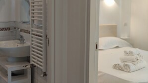 A bathroom with a sink, mirror, towel rack, and a bed with rolled towels. - Sea Dream Palace 2 (Trani)