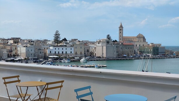 A balcony with two tables and chairs overlooking a harbor with boats and historic buildings. - Sea Dream Palace 2 (Trani)