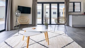 A modern living room with a round table, two wicker chairs, a floor fan, and a TV on the wall. - Casa Monrel, Mambo Beach (Willemstad)